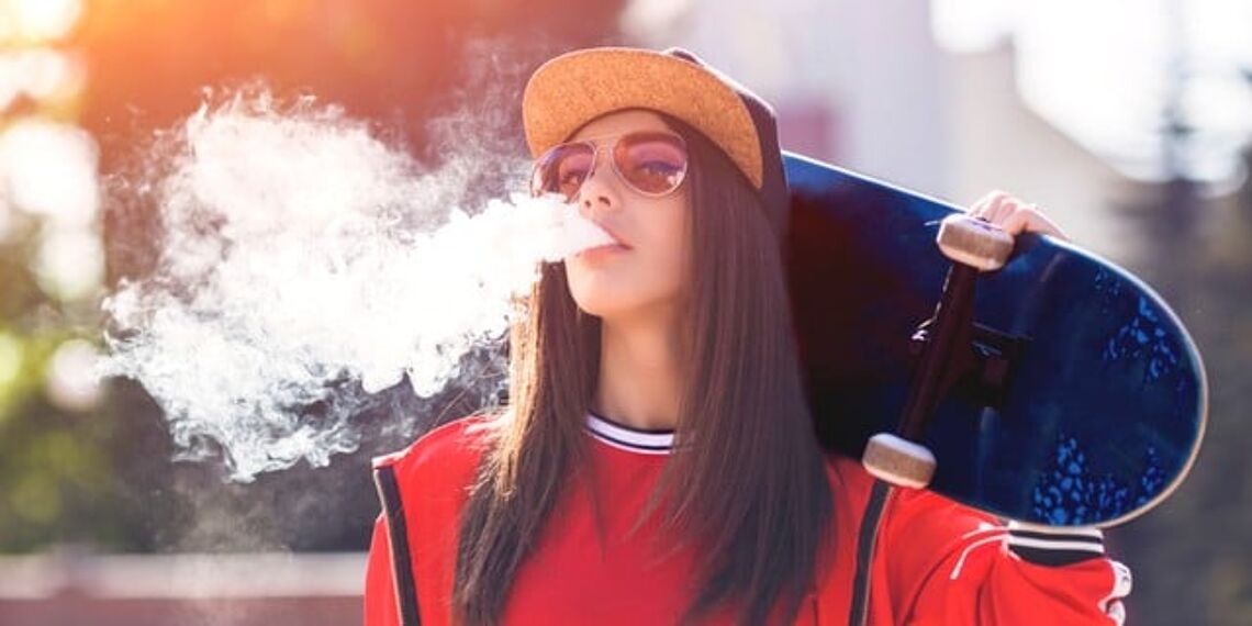 girl with skateboard letting out a huge vape cloud